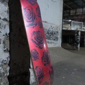 Pink skateboard deck with blue rose patterns leaning against a rough concrete wall in an industrial space.